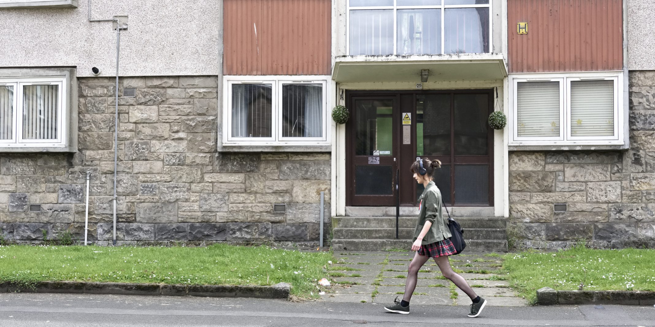Student walking past council flats in poor housing estate with many social welfare problems