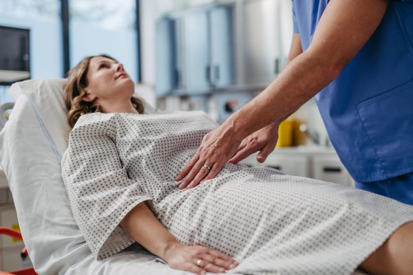 Doctor palpating woman’s abdomen, using hands and steady pressure.