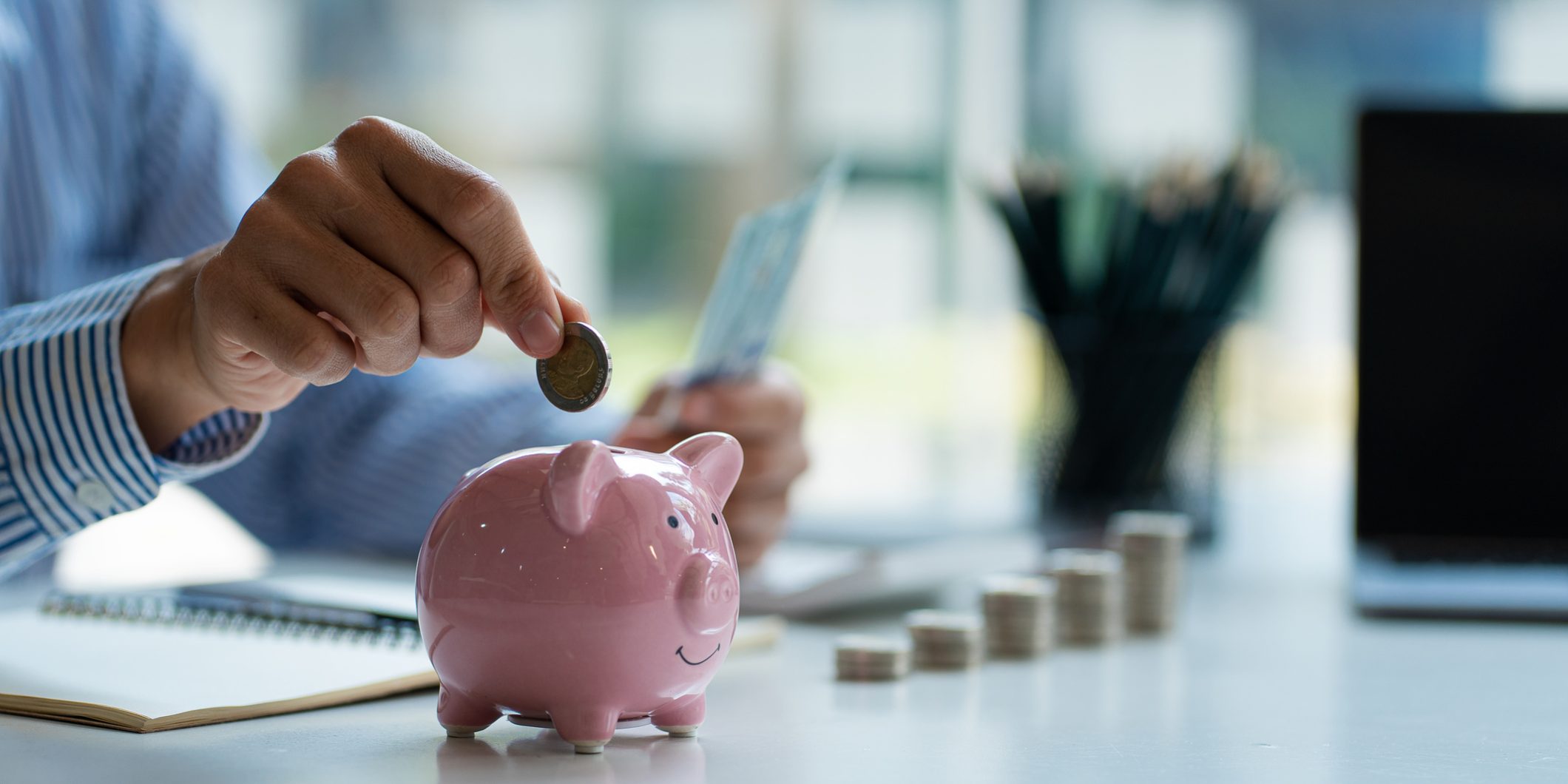 Hands of a young Asian businessman Man putting coins into piggy bank and holding money side by side to save expenses A savings plan that provides enough of his income for payments.