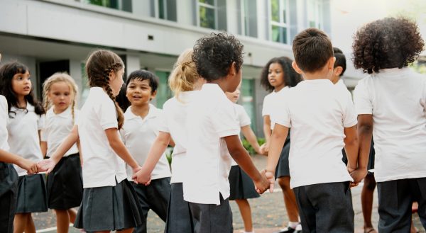 Group of diverse students, boys and girls, holding hands in a circle. Students in school uniforms, diverse children playing outdoors. Diverse students do activities outdoor in school